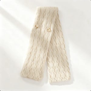 Peut inclure: Écharpe en tricot de couleur crème avec deux boutons ronds et clairs. L'écharpe est pliée en forme de V, mettant en valeur le motif en tricot texturé. La couleur neutre et le design classique suggèrent un accessoire confortable.