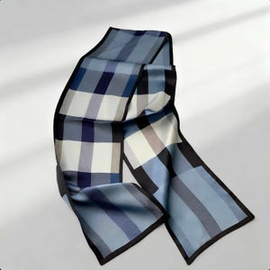 Peut inclure: Une écharpe à carreaux bleus et blancs avec une bordure noire. L'écharpe est en soie et présente un motif de carrés et de rayures dans des tons de bleu, de blanc et de noir. L'écharpe est pliée et drapée.