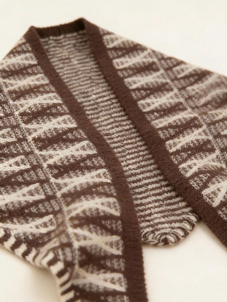 May include: Close-up of a brown and cream-colored cardigan. The knitwear features a geometric pattern with a dark brown border. The fabric appears soft and textured, suitable for cooler weather. The cardigan is folded, showing the collar and part of the sleeves.