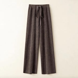 Könnte beinhalten: Braune Hose mit weitem Bein und Kordelzug in der Taille. Die Hose hat ein weiches, strukturiertes Aussehen und eine vertikale Naht auf der Vorderseite jedes Beins. Der Kordelzug hat die gleiche Farbe wie die Hose.