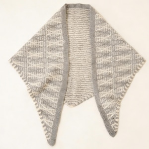 May include: A gray and white knitted shawl with a geometric pattern. The shawl has a triangular shape with a ribbed border and a textured design. The color scheme is neutral, with shades of gray and white, making it a versatile accessory.