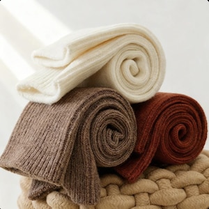 May include: A stack of rolled-up, ribbed knit socks in cream, brown, and rust colors. The socks are neatly arranged, showcasing their texture and the variations in shades. The image highlights the cozy and warm appearance of the socks.
