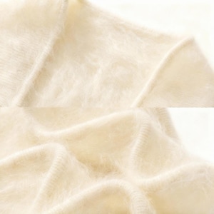 Peut inclure: Gros plan sur un pull en tricot cr&egrave;me et duveteux. Le tissu a un aspect doux et textur&eacute; avec des coutures visibles le long des coutures. Le pull semble &ecirc;tre fait d'un m&eacute;lange d&eacute;licat, peut-&ecirc;tre de laine ou de mohair.