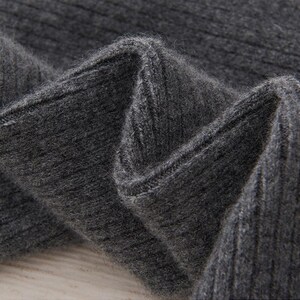 May include: Close-up of a section of dark gray ribbed knit fabric. The fabric is folded, showing the texture and the way the light plays across the surface. The knit has a soft, slightly fuzzy appearance.