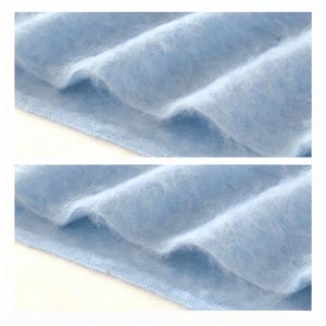 Peut inclure: Gros plan sur un tissu bleu clair et doux avec une texture floue. Le tissu est pli&eacute;, cr&eacute;ant des vagues et des ombres douces. Le mat&eacute;riau semble &ecirc;tre un textile d&eacute;licat en tricot ou tiss&eacute;, peut-&ecirc;tre une &eacute;charpe ou un ch&acirc;le.