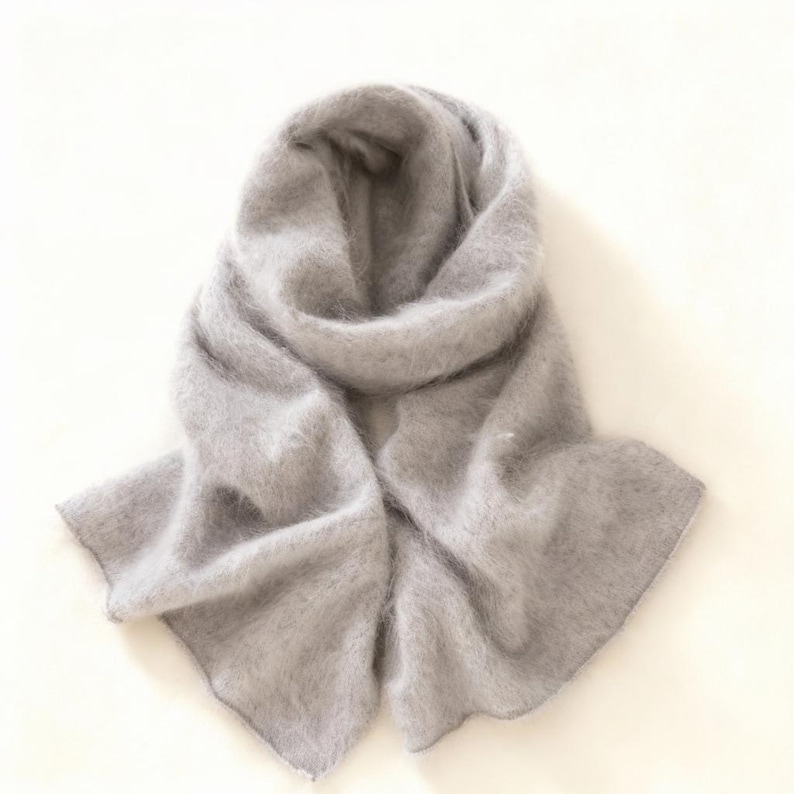 Peut inclure: Une &eacute;charpe gris clair en mati&egrave;re duveteuse. L'&eacute;charpe est drap&eacute;e et pli&eacute;e, avec une texture floue. L'&eacute;charpe est de couleur unie et semble &ecirc;tre faite d'une mati&egrave;re chaude, adapt&eacute;e au temps froid.