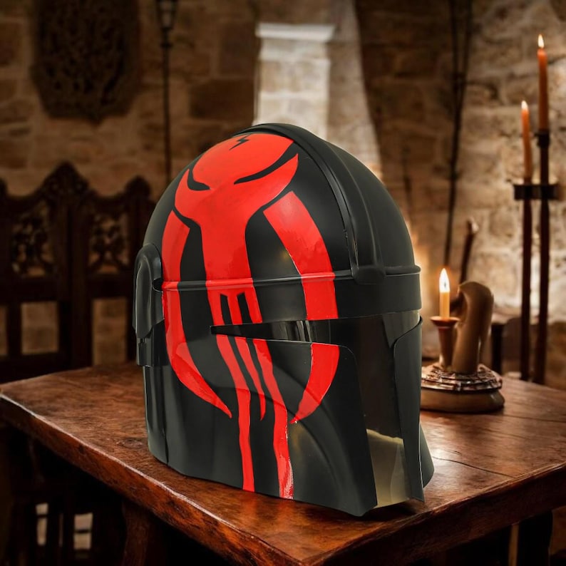 May include: A black helmet featuring a prominent red graphic design on the front. The helmet has a smooth, curved surface with a horizontal visor opening and a distinct T-shaped faceplate structure, showcasing a bold, stylized red emblem.