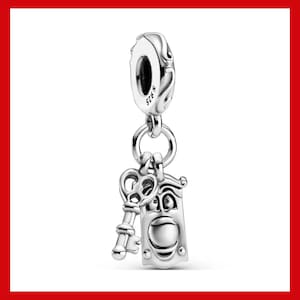 May include: A silver charm featuring a key and a door with a face. The charm is suspended from a larger silver piece with a hole. The key and door are detailed with intricate designs, and the charm is likely made of sterling silver.