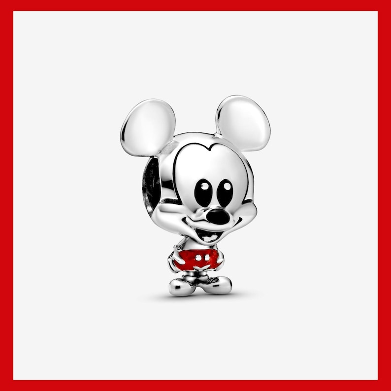 May include: A silver charm featuring Mickey Mouse with large round ears, a smiling face, and red shorts with white polka dots. The charm is a detailed, three-dimensional design.