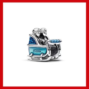 May include: A silver charm featuring two figures in a blue and silver sleigh. The sleigh has blue accents and the words "WORLD OF FROZEN" are visible. The charm is likely a collectible item or jewelry.