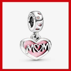 May include: A silver charm with the word "MOM" in a heart-shaped pendant. The heart has a pink enamel fill and a silver border. The charm has a loop with the brand name "PANDORA" engraved on it, and is decorated with small pink hearts.