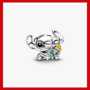Puede incluir: Un charm de plata que representa al personaje Stitch de Lilo & Stitch. Stitch gui&ntilde;a un ojo y sostiene un objeto verde y rosa con una mariposa amarilla. El charm es detallado y tiene un acabado pulido.
