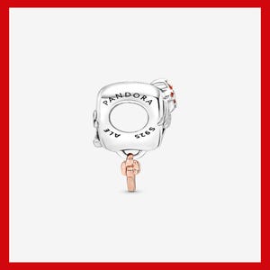 May include: A silver charm with the word "PANDORA" engraved on it. The charm has a key pendant in rose gold and small red accents. The charm is marked with "ALE" and "S925".