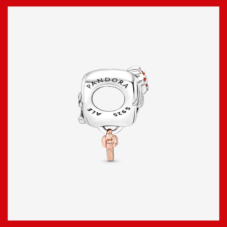 May include: A silver charm with the word "PANDORA" engraved on it. The charm has a key pendant in rose gold and small red accents. The charm is marked with "ALE" and "S925".