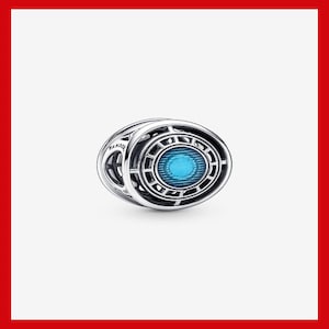 May include: A silver charm with an oval, geometric design. The center features a bright blue, circular stone. The charm has a detailed, openwork pattern and the word "Pandora" is visible on the side.