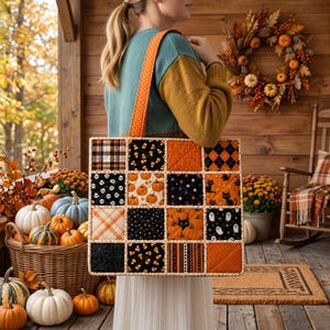 Könnte beinhalten: Eine gesteppte Tragetasche mit einem Patchwork-Design aus sechzehn quadratischen Stoffbahnen mit Halloween-Motiven wie Kürbissen, Geistern, schwarzen Katzen, Totenköpfen, Zuckermais und Karomustern, ergänzt durch einen orangefarbenen Schulterriemen.