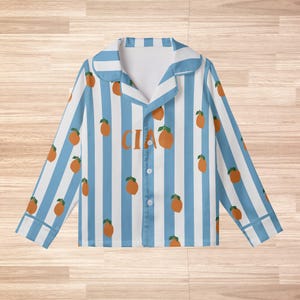 May include: Blue and white striped pajama top with orange fruit illustrations. The word "CIAO" is printed in orange on the front. The pajama top has a collared neckline and button-down front.
