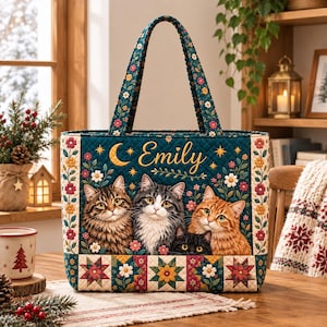 May include: A quilted tote bag in dark teal featuring a printed design of four cats, a crescent moon, and stars. The name Emily is written in gold script. The bag is decorated with colourful floral borders and a geometric star pattern at the base.