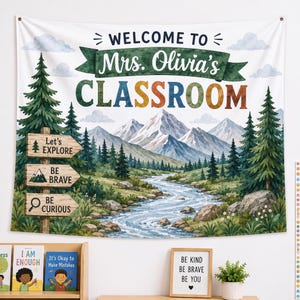 May include: A fabric wall tapestry featuring a mountain landscape with a river, pine trees, and a wooden signpost. The text reads: WELCOME TO Mrs. Olivia's CLASSROOM, Let's EXPLORE, BE BRAVE, and BE CURIOUS. The design includes watercolor-style clouds.