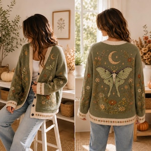 May include: An olive green knit cardigan featuring a large moth graphic on the back, surrounded by floral and celestial motifs including a crescent moon. The front displays matching floral embroidery, a button-down closure, and cream trim.