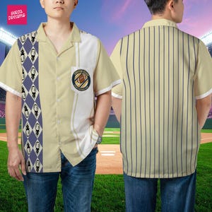 K&ouml;nnte beinhalten: Kurz&auml;rmeliges Button-Down-Shirt mit Fu&szlig;ballmotiv. Das Hemd ist &uuml;berwiegend beige mit wei&szlig;en und blauen Akzenten. Die Vorderseite hat ein Rautenmuster und eine Tasche mit einem Fu&szlig;ballclub-Logo. Die R&uuml;ckseite hat vertikale blaue Streifen.