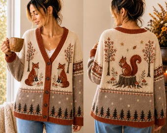 May include: A beige and grey knit cardigan featuring a button-down front, long sleeves, and a woodland-themed pattern. The design includes illustrations of foxes, a squirrel on a tree stump, pine trees, mushrooms, and snowflakes in brown tones.