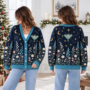 May include: A navy blue V-neck cardigan featuring a teal moth graphic, yellow crescent moons, and stars on the upper portion, with a lower pattern of white, pink, and blue wildflowers. The garment has a teal ribbed trim and five buttons.