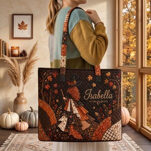 May include: A quilted tote bag featuring a dark brown background with an autumn-themed design of a witch with long red hair, surrounded by fall foliage and the name Isabella in script. The bag has two matching patterned shoulder straps.