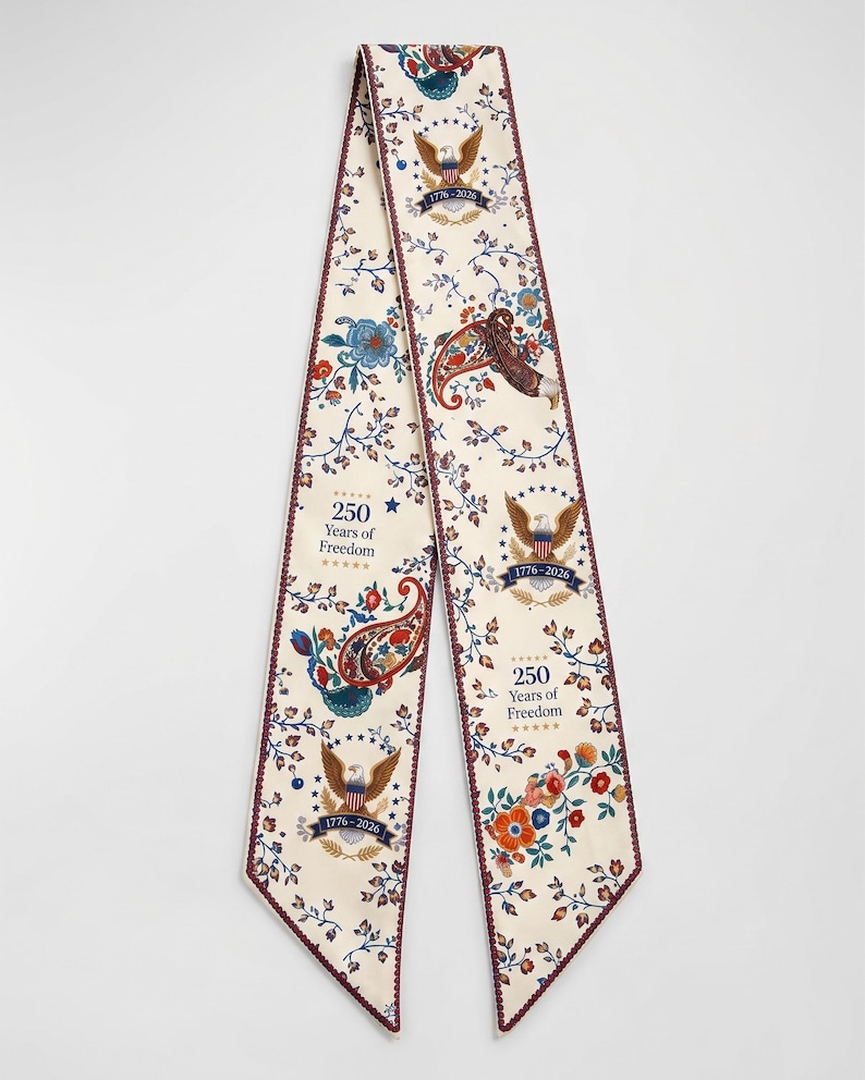 May include: Cream-colored scarf with a repeating floral and paisley pattern. The scarf features the text "250 Years of Freedom" and the years "1776-2026", along with images of eagles. The edges are trimmed with a dark red border.