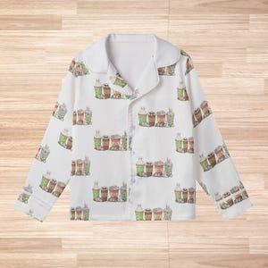 May include: White pajama top with a repeating pattern of Easter-themed drinks, including coffee and milkshakes, in shades of green, brown, and pink. The pajamas have a collared neckline and button-down front.