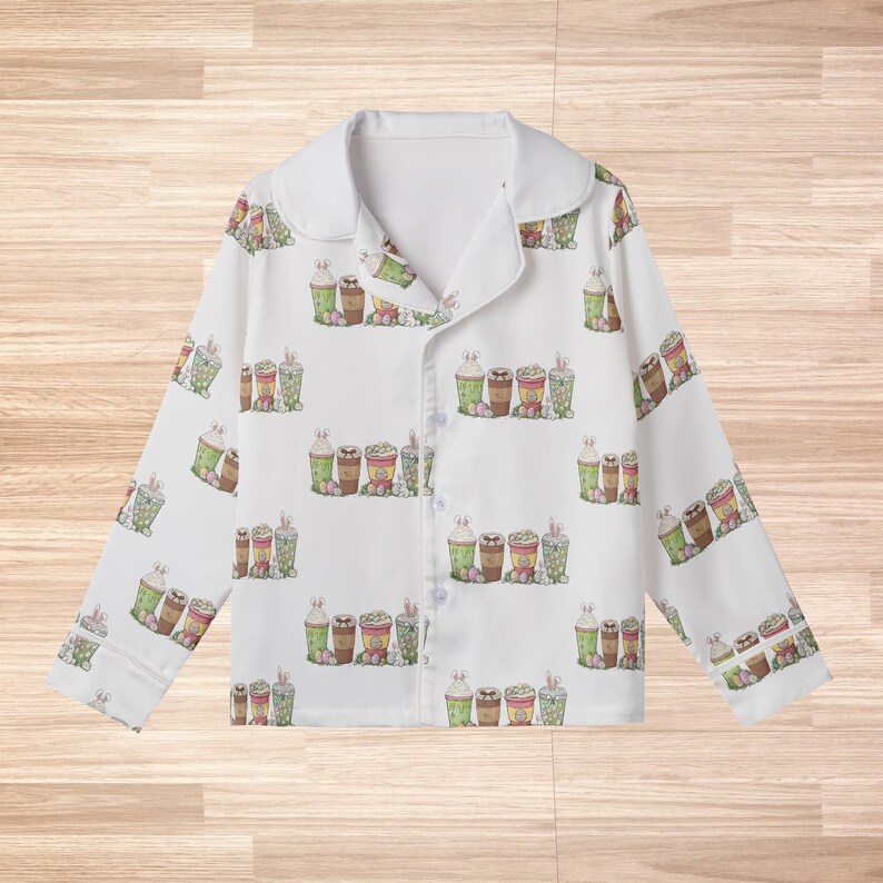 May include: White pajama top with a repeating pattern of Easter-themed drinks, including coffee and milkshakes, in shades of green, brown, and pink. The pajamas have a collared neckline and button-down front.