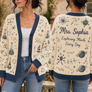 May include: A cream-colored button-down cardigan with dark blue trim, featuring a science-themed print of molecules, planets, and laboratory equipment. The back displays the text "Mrs. Sophia Exploring Minds Every Day" alongside "E=mc2" and "H2SO4" chemical formulas.