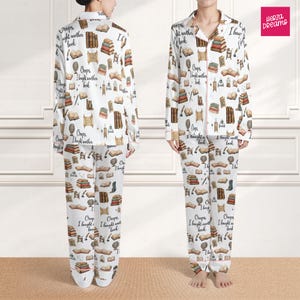 May include: A white ceramic mug with a black handle and the text "But First, Coffee" in a bold, black font. The mug is set against a blurred background, suggesting a cozy setting.