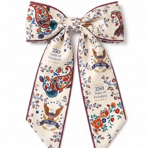 May include: Cream-colored bow tie with a paisley and floral pattern. The bow tie features the text "250 Years of Freedom" and an eagle emblem. The edges are trimmed with a dark red border.