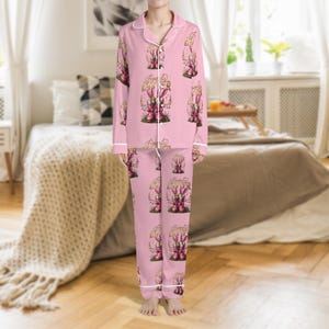 May include: Pink pajama set with a repeating pattern of Easter bunnies, eggs, and the text "Happy Easter". The pajamas have white trim and a button-down top. The long-sleeved top and pants are made of a soft material.