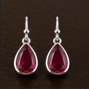 May include: A pair of silver teardrop earrings with large, faceted, deep red gemstones. The earrings have a simple, elegant design with a hook closure. The gemstones are set in a polished silver bezel.