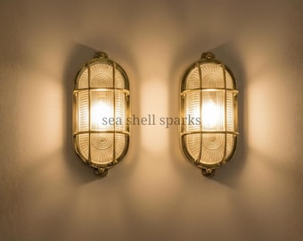 May include: Two brass-colored, oval-shaped wall sconces with a grid pattern over the glass. The sconces are lit, casting a warm glow on the wall. The text "sea shell sparks" is visible.