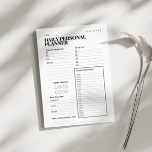 Könnte beinhalten: Ein weißer täglicher persönlicher Planer mit schwarzem Text. Der Planer enthält Abschnitte für Prioritäten, To-Do-Listen, Notizen, einen Wassertracker, einen Mahlzeiten-Tracker und einen Zeitplan. Der Text "DAILY PERSONAL PLANNER" steht oben.