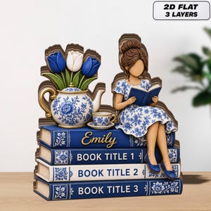 May include: A decorative wooden sculpture featuring a woman reading on a stack of books. The books are blue with white text, and the sculpture includes a teapot, teacup, and flowers. The text "2D FLAT 3 LAYERS" is in the upper right corner.