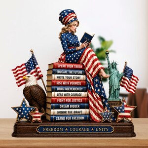 May include: A patriotic figurine featuring a woman in a star-spangled dress and head wrap, reading a book while seated atop a stack of books. The books display inspirational phrases. Includes an American flag, an eagle, the Statue of Liberty, and star-shaped decorations.