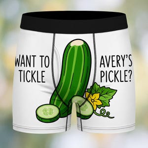 May include: White boxer briefs with a black waistband. The front features a cartoon cucumber with the text "WANT TO TICKLE" on the left and "AVERY'S PICKLE?" on the right. The cucumber has green and white stripes.