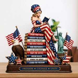 May include: A patriotic statue featuring a woman in a dress and head wrap adorned with the American flag design, reading a book. The statue includes a bald eagle, the Statue of Liberty, and American flags. The base reads "Freedom, Courage, Unity."