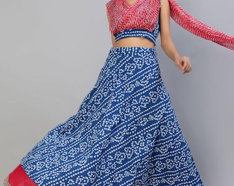 May include: A two-piece ensemble featuring a sleeveless blue crop top and a matching floor-length skirt, both adorned with a white tie-dye pattern. The skirt includes a solid pink hem with gold trim, paired with a matching red and white scarf.