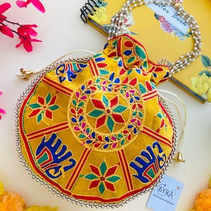 Può includere: Pochette ricamata gialla con chiusura a coulisse. La pochette presenta un motivo floreale centrale rosso, blu e verde, circondato da un bordo di perline. È attaccata un'etichetta con il marchio "BYRA".