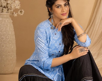 May include: A light blue tunic featuring a white intricate floral pattern, three-quarter sleeves, and a central row of dark buttons, paired with black wide-leg trousers that have thin blue and gold horizontal stripes along the lower hemline.