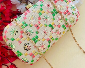Può includere: Pochette rettangolare color crema con un motivo intrecciato rosa, verde e giallo. Presenta ricami floreali e una tracolla a catena dorata. La chiusura è dorata.