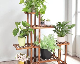 May include: A multi-tiered, wooden plant stand with various potted plants. The stand is made of dark brown wood and has multiple shelves of different sizes. The plants include green leafy plants and flowering plants, creating a natural aesthetic.