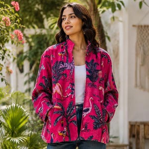 Puede incluir: Una chaqueta de manga larga de color rosa brillante con un estampado de animales tropicales en azul oscuro y blanco, sobre una camiseta sin mangas blanca, vaqueros azules y zapatillas blancas. La chaqueta tiene cuello alto y cremallera.
