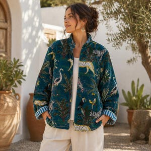 May include: Teal velvet jacket with a vibrant jungle print featuring leopards, birds, and foliage. The jacket has a stand-up collar, long sleeves, and a blue and white striped cuff detail. The jacket is open, revealing a white top.