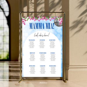 May include: A gold metal framed seating chart with the words "MAMMA MIA!" and "Look who's here!" in blue. The chart has a blue background with a floral design and a disco ball. The names of the guests are listed below.
